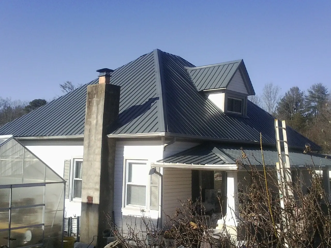 Dark blue standing seam metal roof on a white farmhouse with dormer — Slate & Tile Roof Repair by Roofing Brothers in Dry Branch