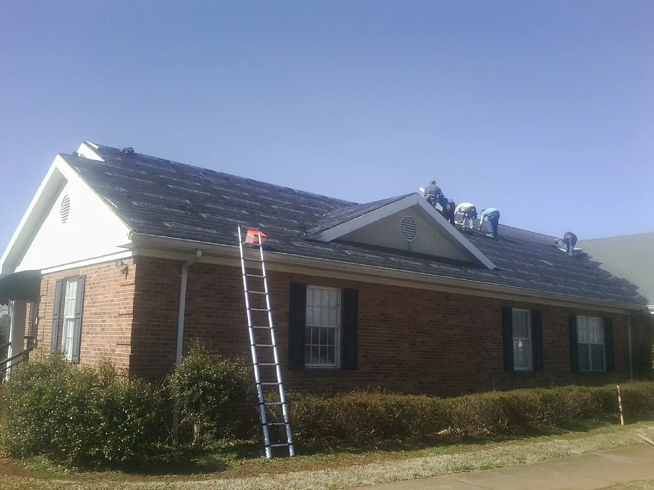 Crew tearing shingles off a brick ranch roof with a ladder set — Emergency Roof Repair work by our crew in Dry Branch