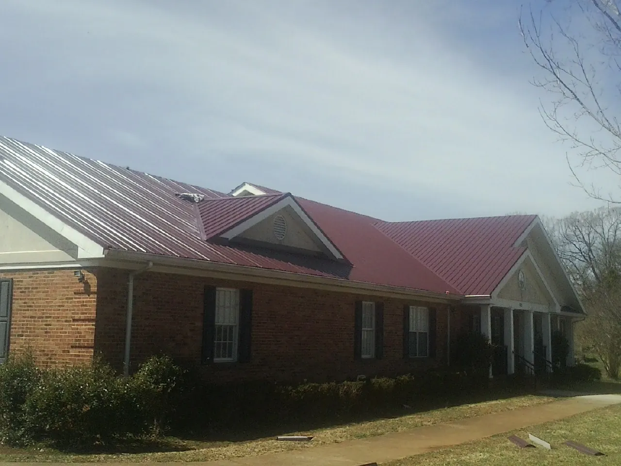 Red metal roof with gabled entries on a long brick building, from a Hail Damage Roof Repair job in Dry Branch