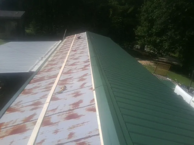 Old rusted panels beside newly installed green metal roofing — Wind Damage Roof Repair by Roofing Brothers in Dry Branch