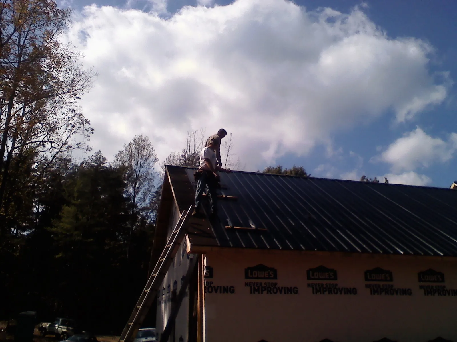Roofer fastening dark metal panels high against a cloudy sky, from a Roof Inspection job in Dry Branch