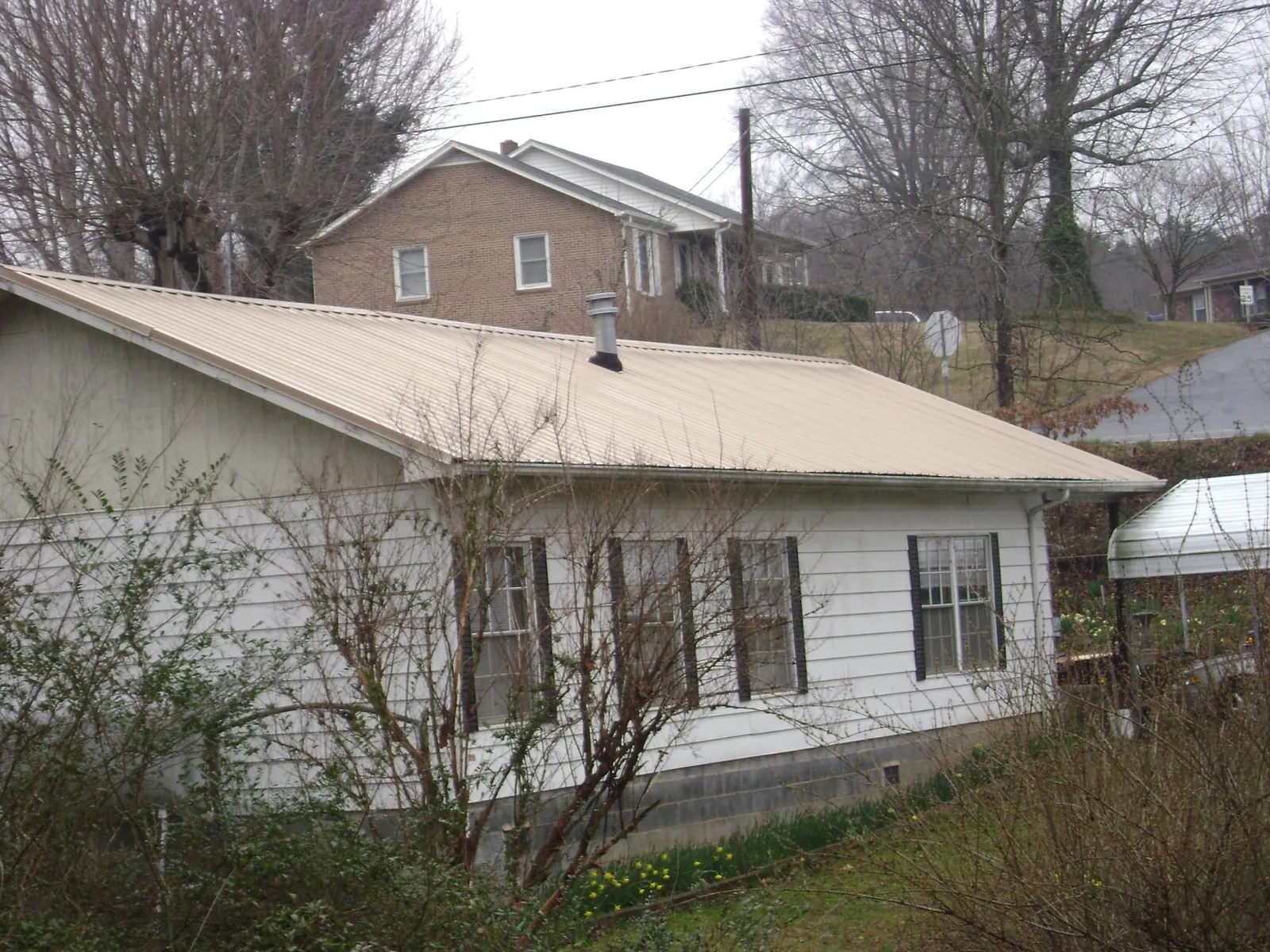 Tan metal roof on a white sided house set into a hillside — Commercial Roofing by Roofing Brothers in Dry Branch