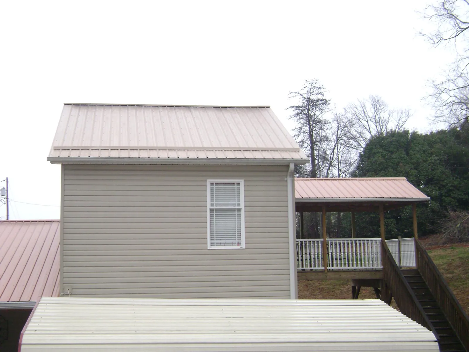 Tan metal roofs on a two story addition and attached porch, from a Roof Replacement job in Dry Branch